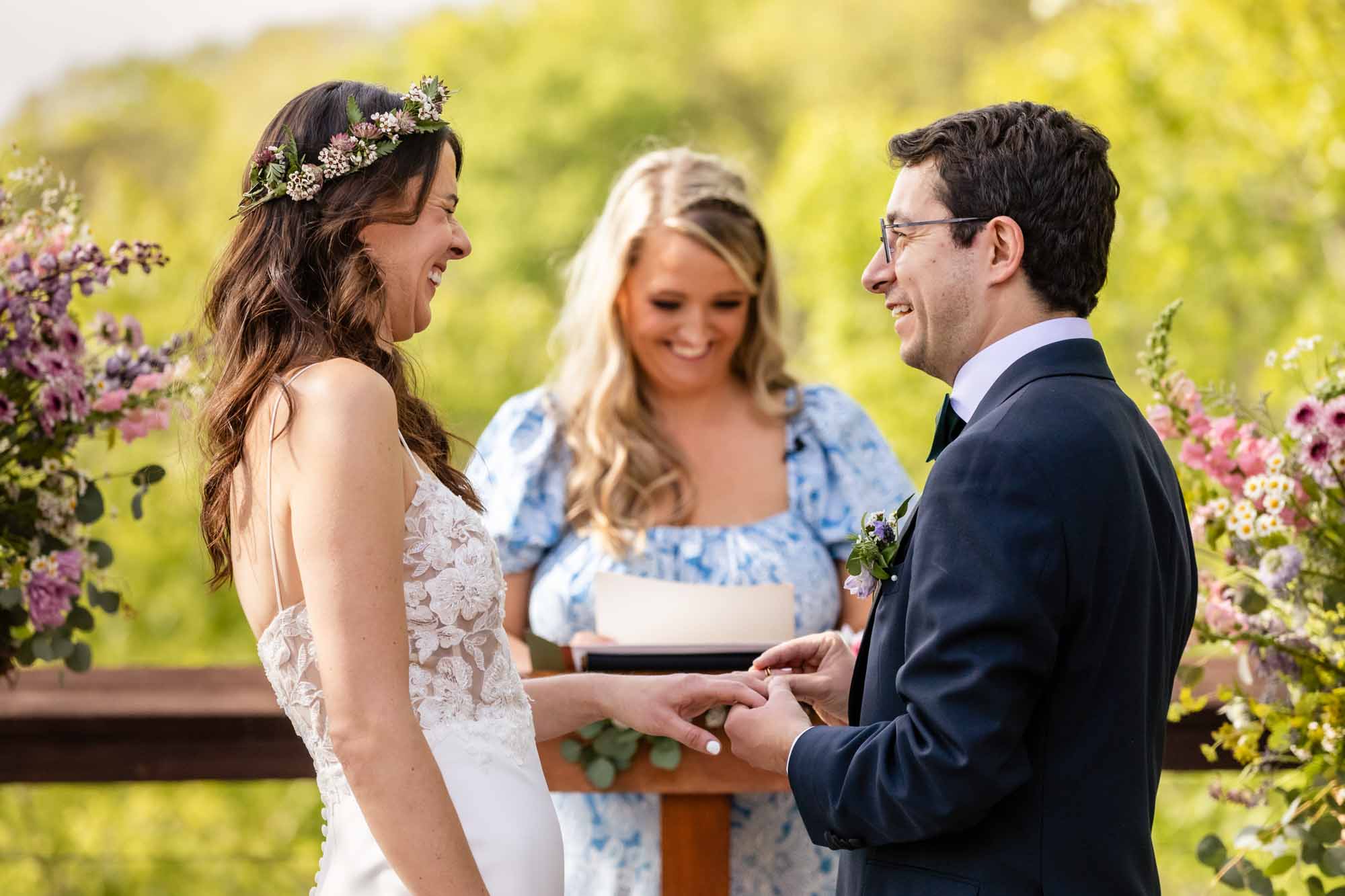 bride and groom laugh together as they put their rings on during their outdoor wedding ceremony, captured by photojournalist wedding photographer Pamela Anticole
